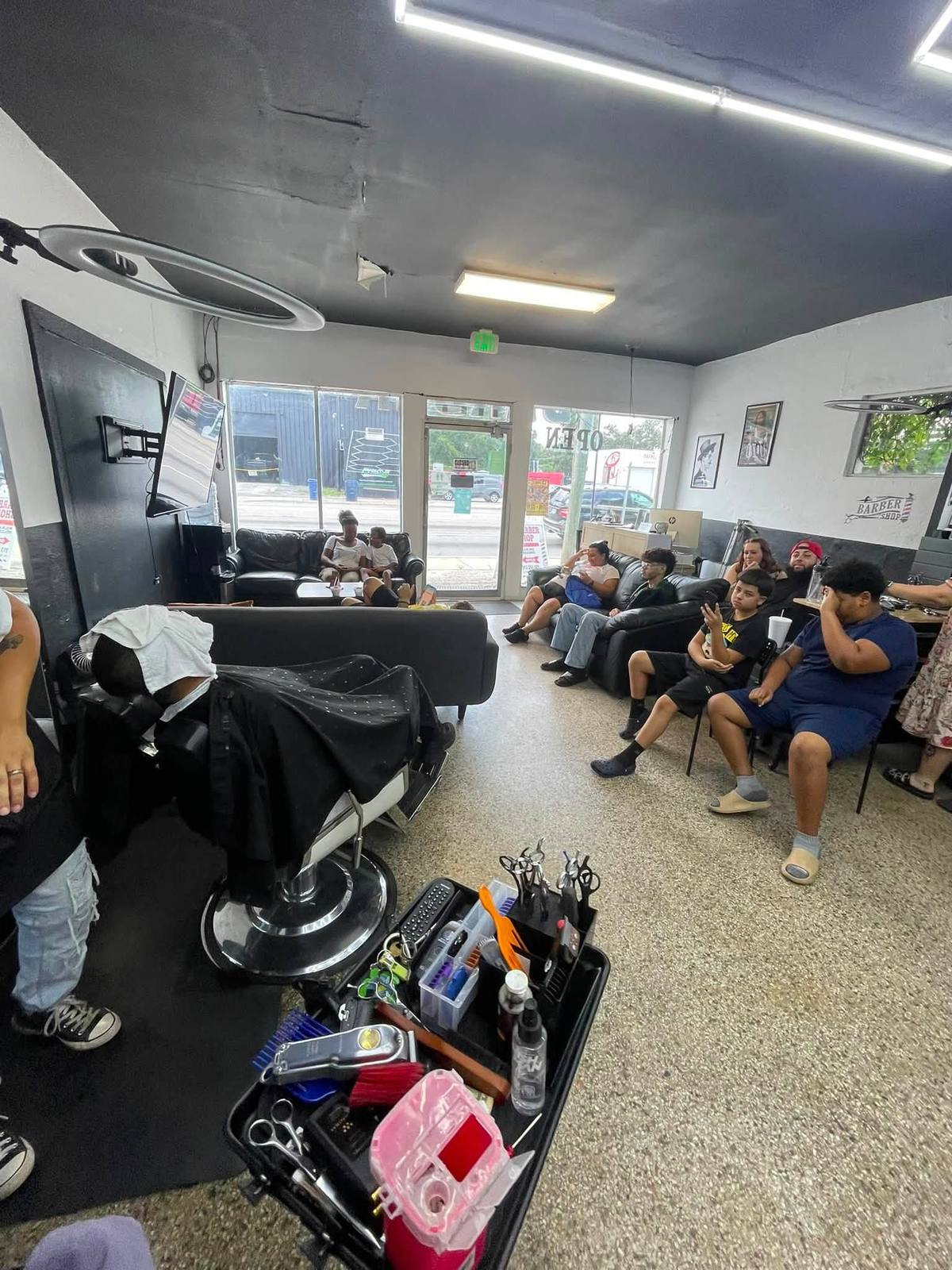 Inside the shop looking down the floor: black ceiling, white walls with a black wainscot band, speckled terrazzo, leather sofas full of waiting families, and the glass storefront onto N. Nebraska Ave.