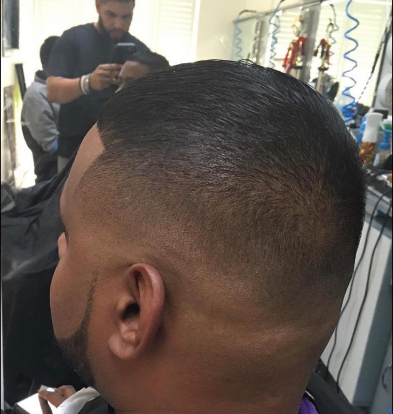 Rear three-quarter view of a high skin fade with a slicked-back top and a shaped beard.