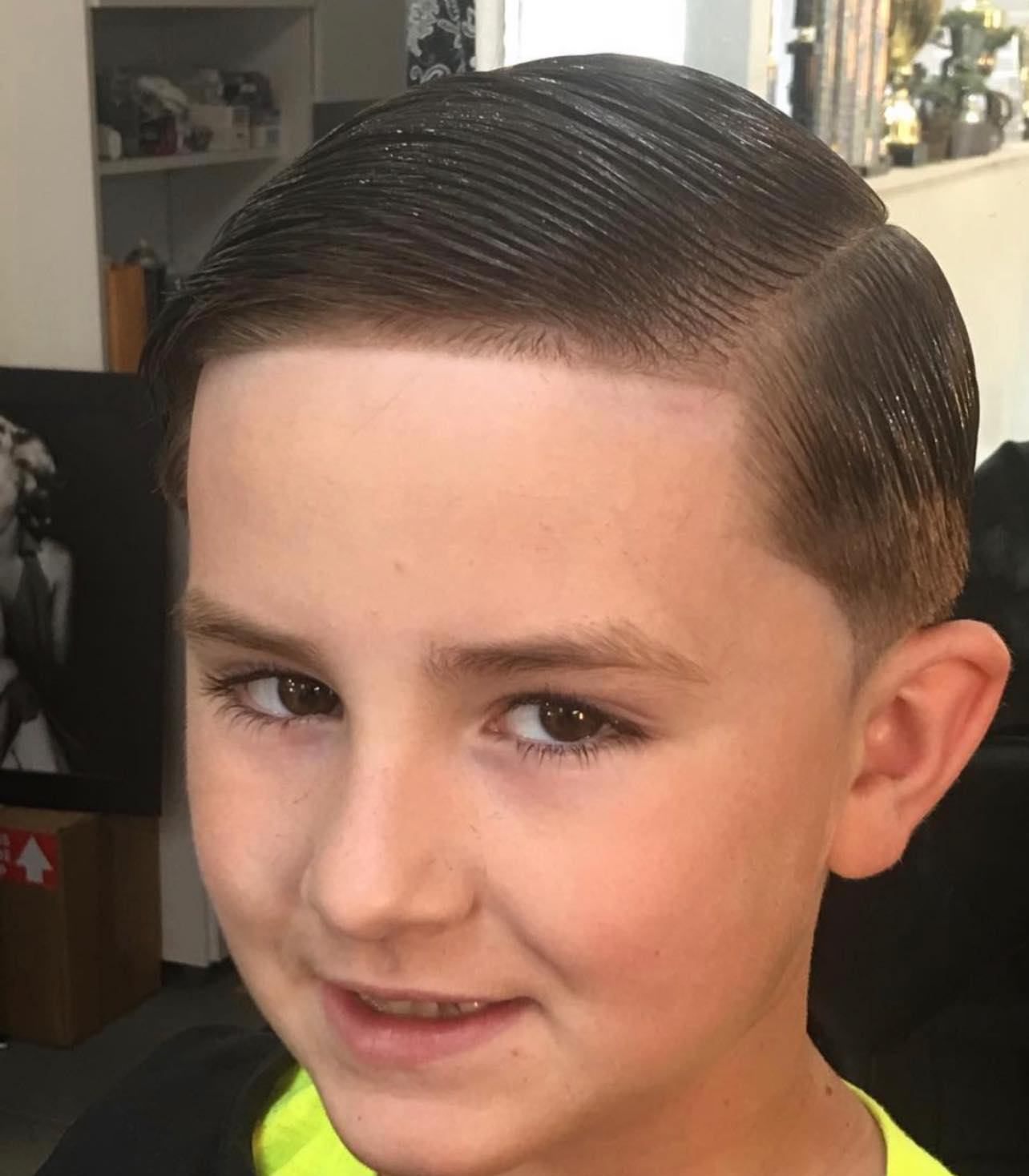 Boy with a slicked side part and tapered sides, finished and styled in the chair.