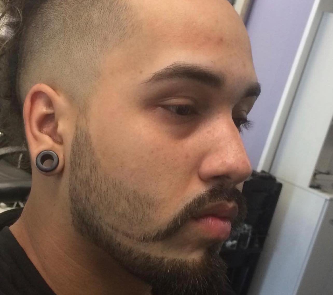 Profile of a high skin fade with a man-bun top and a sharply carved beard line.